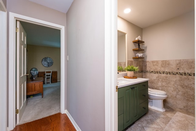 bathroom with toilet, tile walls, vanity, and wainscoting