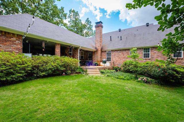 rear view of property featuring a yard, a shingled roof, a chimney, and brick siding