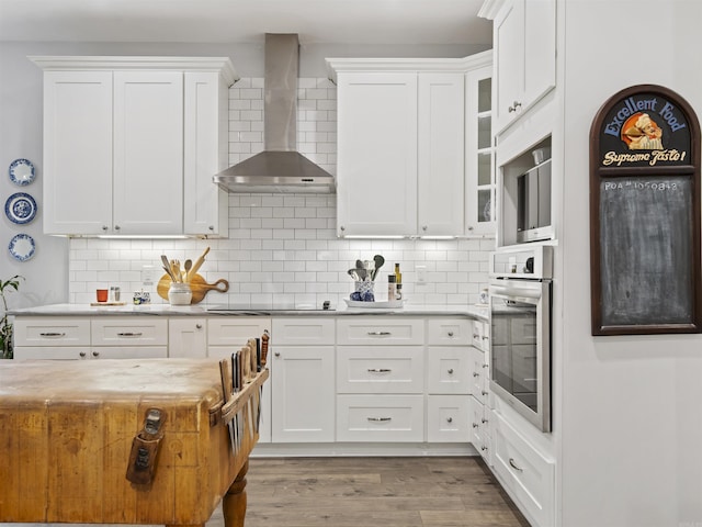 kitchen with oven, wall chimney range hood, backsplash, and white cabinets