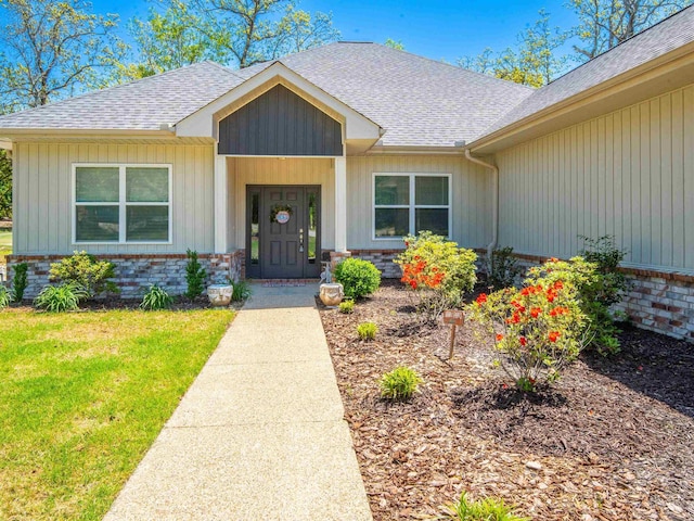 property entrance with a shingled roof, brick siding, and a lawn