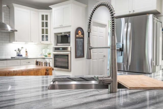 kitchen featuring glass insert cabinets, white cabinetry, backsplash, wall chimney range hood, and appliances with stainless steel finishes