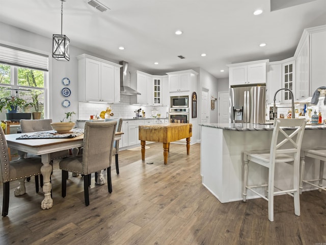 kitchen featuring stainless steel appliances, tasteful backsplash, visible vents, wall chimney exhaust hood, and glass insert cabinets
