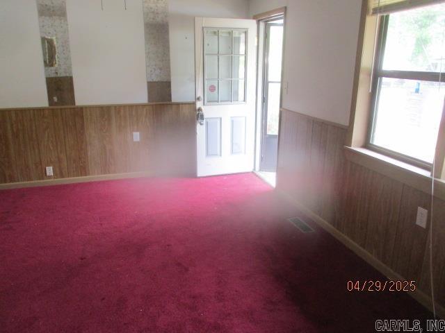 unfurnished room featuring wainscoting, wood walls, a wealth of natural light, and visible vents