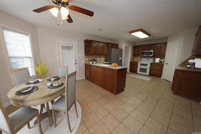 kitchen featuring a peninsula, light tile patterned floors, a sink, stainless steel appliances, and tasteful backsplash