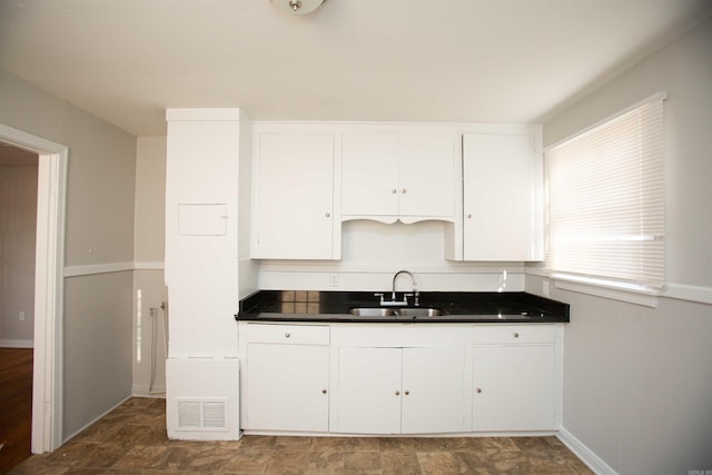 2919 W 27th St, Little Rock, AR 72204 - kitchen with a sink, dark countertops, white cabinets, visible vents, and baseboards