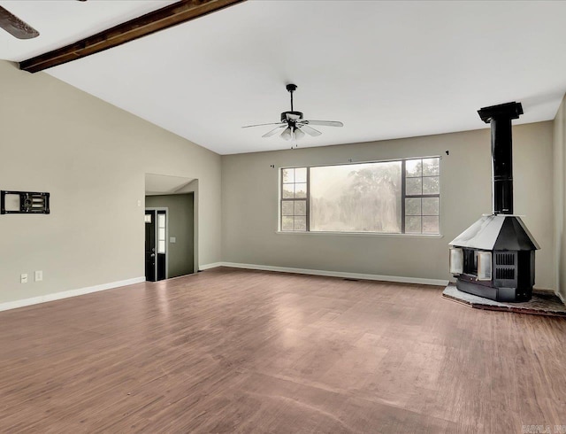 unfurnished living room with a wood stove, lofted ceiling with beams, a ceiling fan, and wood finished floors