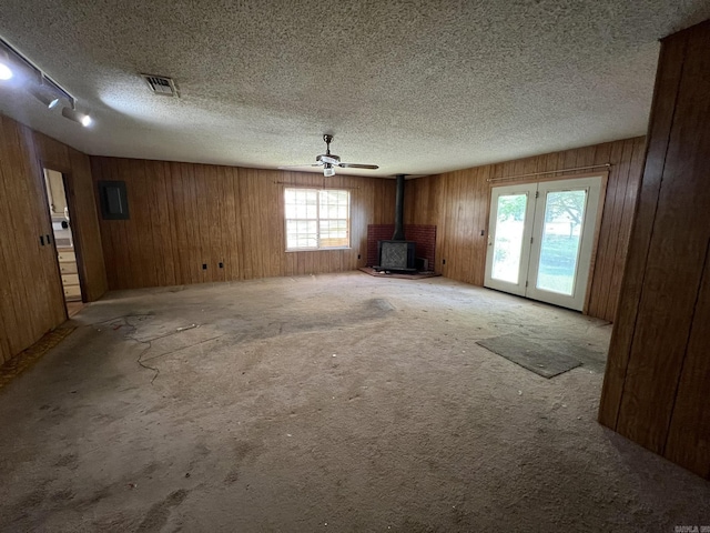 unfurnished living room featuring carpet floors, a textured ceiling, visible vents, a wood stove, and wooden walls