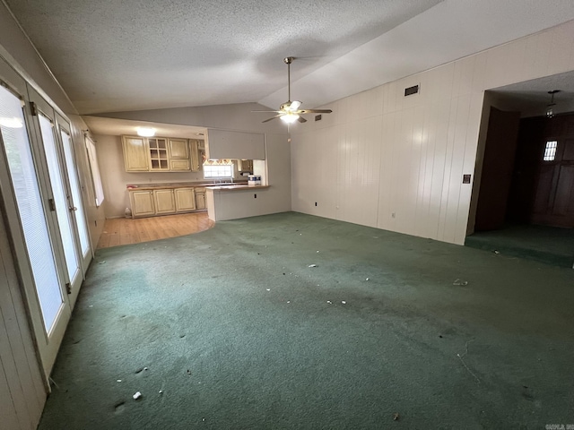 unfurnished living room featuring lofted ceiling, a textured ceiling, visible vents, ceiling fan, and light carpet