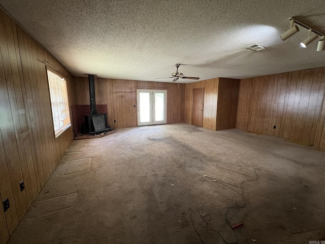 unfurnished living room with wood walls, a wood stove, a textured ceiling, visible vents, and a ceiling fan