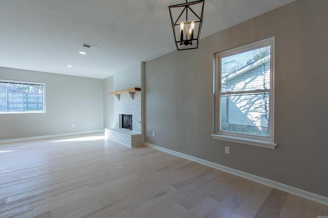 unfurnished living room featuring light wood finished floors, a chandelier, visible vents, and a brick fireplace