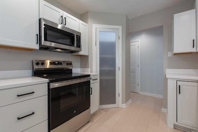 kitchen featuring light wood finished floors, stainless steel appliances, light countertops, and white cabinets