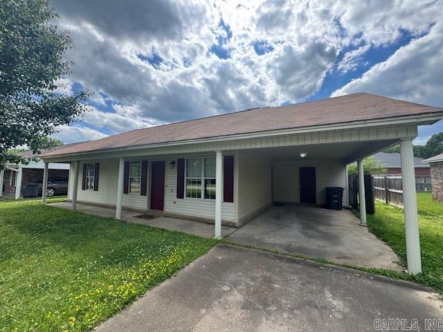 ranch-style house featuring driveway, an attached carport, a front lawn, and fence