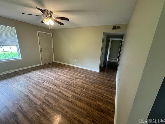 unfurnished room with baseboards, ceiling fan, visible vents, and dark wood-type flooring