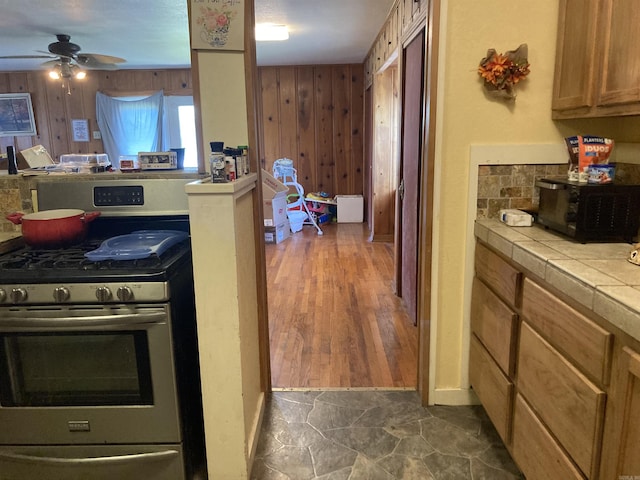 207 11th St, Mena, AR 71953 - kitchen featuring stainless steel range with gas cooktop, tile countertops, black microwave, wood walls, and decorative backsplash