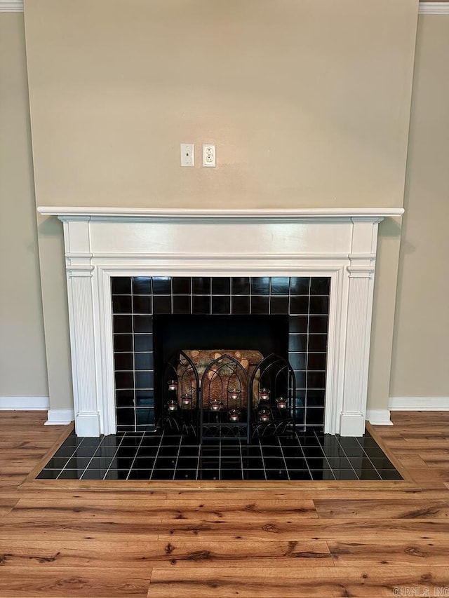 interior details with baseboards, a tiled fireplace, and wood finished floors