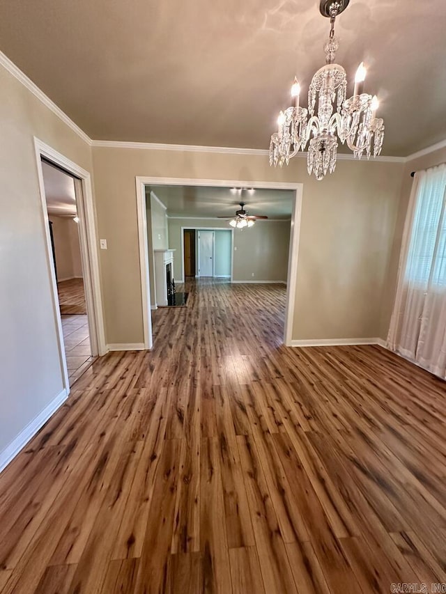 unfurnished dining area featuring crown molding, baseboards, wood finished floors, and ceiling fan with notable chandelier