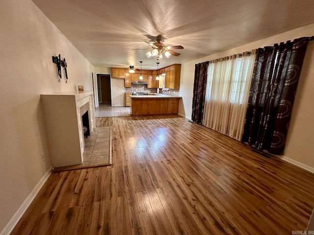 kitchen with hardwood / wood-style flooring, brown cabinetry, under cabinet range hood, open floor plan, and a ceiling fan