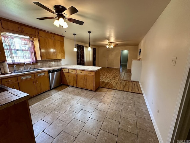 kitchen with a ceiling fan, tile countertops, dishwasher, a sink, and a peninsula