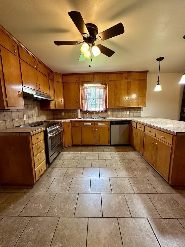 kitchen with under cabinet range hood, brown cabinetry, a sink, a peninsula, and stainless steel appliances