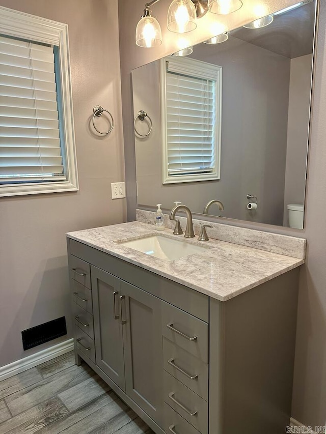 half bath featuring vanity, baseboards, visible vents, and wood finished floors