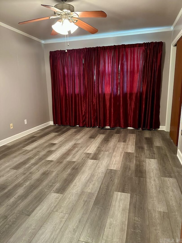 spare room featuring a ceiling fan, baseboards, crown molding, and wood finished floors