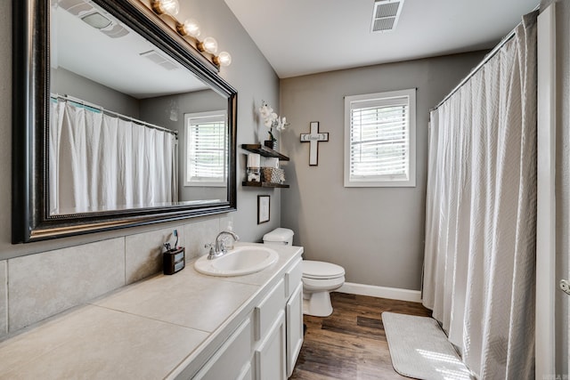 full bath with toilet, a healthy amount of sunlight, visible vents, and wood finished floors