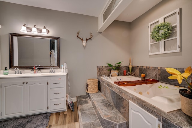 full bathroom featuring double vanity, a jetted tub, wood finished floors, and a sink