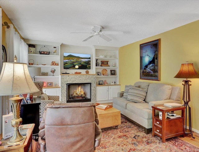 living area with baseboards, light wood finished floors, ceiling fan, built in features, and a high end fireplace