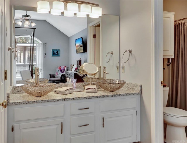 full bath with a sink, toilet, vaulted ceiling, ceiling fan, and double vanity