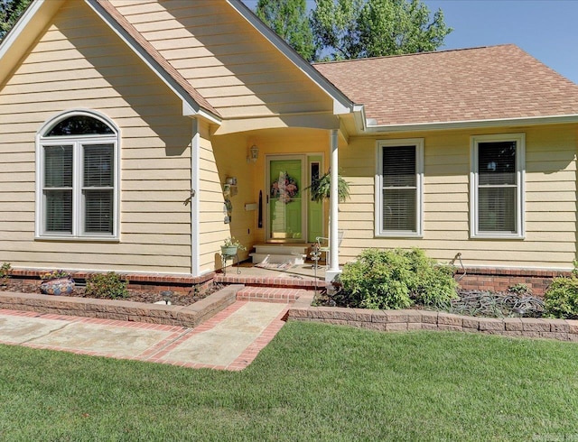 view of exterior entry with a yard and a shingled roof