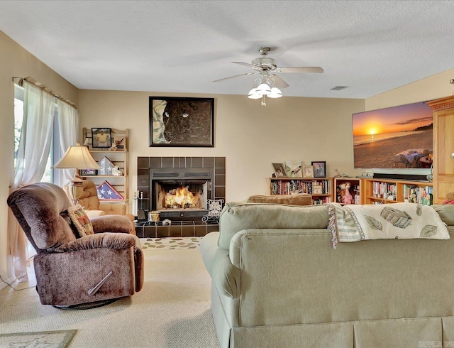 carpeted living room featuring ceiling fan, a tiled fireplace, and visible vents