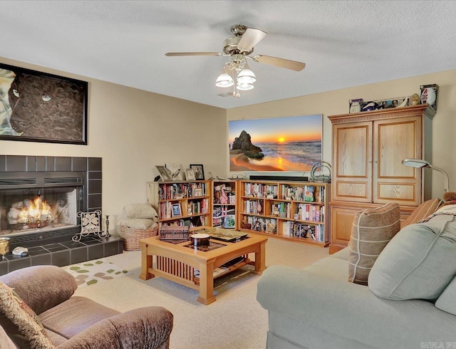 living area with ceiling fan, a textured ceiling, and a tiled fireplace