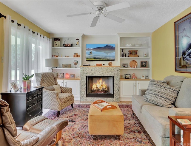 living room with a ceiling fan, a textured ceiling, a high end fireplace, and built in features
