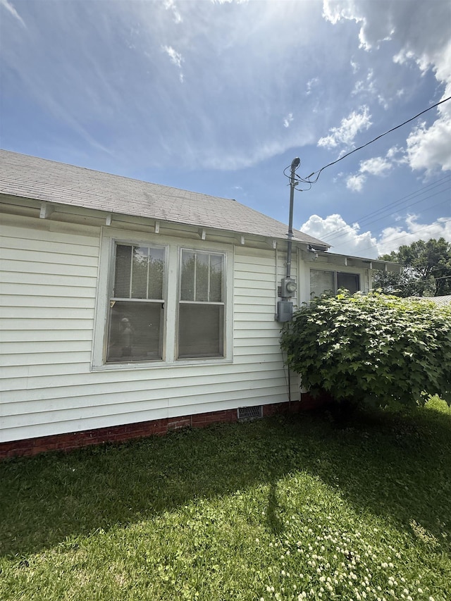 view of side of property with roof with shingles and a lawn