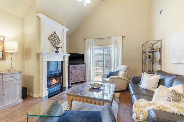 living room featuring a ceiling fan, visible vents, high vaulted ceiling, wood finished floors, and a tile fireplace