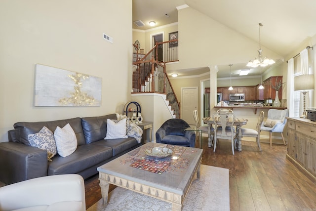 living room with a notable chandelier, wood-type flooring, stairs, crown molding, and high vaulted ceiling