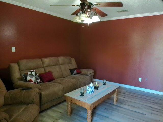 living area featuring baseboards, light wood finished floors, ceiling fan, visible vents, and crown molding