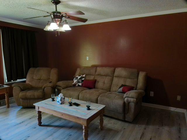living room featuring ceiling fan, ornamental molding, a textured ceiling, and wood finished floors