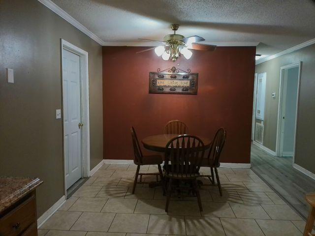 dining space featuring ceiling fan, a textured ceiling, light tile patterned flooring, and ornamental molding