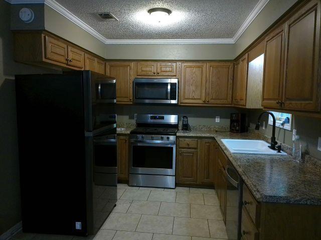 kitchen featuring a sink, stainless steel appliances, brown cabinetry, crown molding, and light tile patterned floors