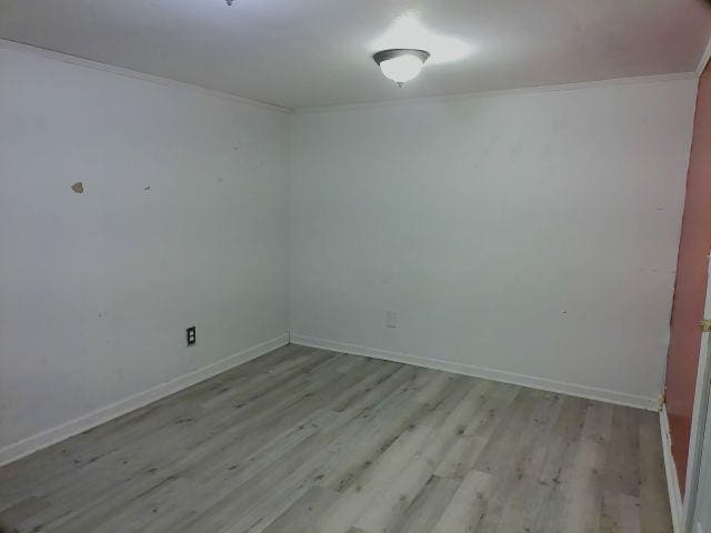 empty room featuring crown molding, baseboards, and light wood-style floors
