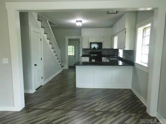 kitchen with a peninsula, a sink, dark countertops, baseboards, and black appliances