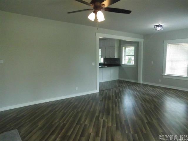 unfurnished living room with a wealth of natural light, dark wood-style flooring, baseboards, and a ceiling fan