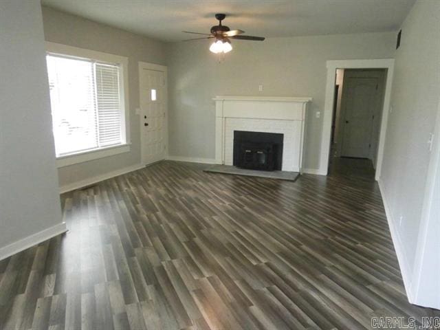 unfurnished living room featuring baseboards, a brick fireplace, dark wood finished floors, and a ceiling fan
