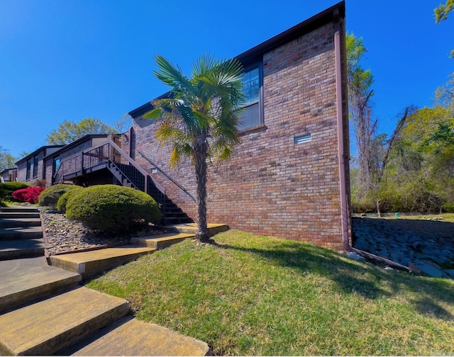view of home's exterior with a yard, stairs, a wooden deck, and brick siding