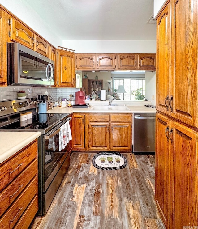 kitchen with a sink, brown cabinetry, dark wood finished floors, and appliances with stainless steel finishes