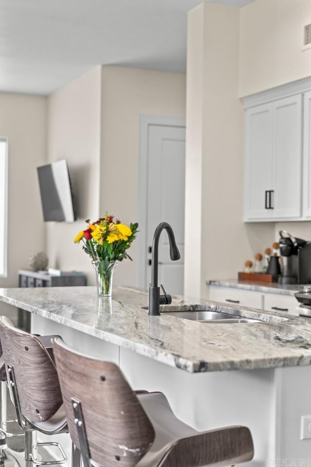 920 Park St, Little Rock, AR 72202 - kitchen featuring light stone counters, white cabinets, a sink, and a kitchen bar