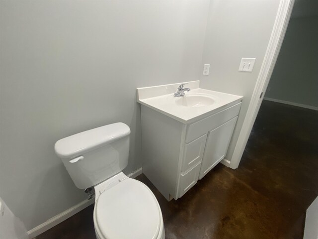 half bathroom with toilet, baseboards, vanity, and concrete floors
