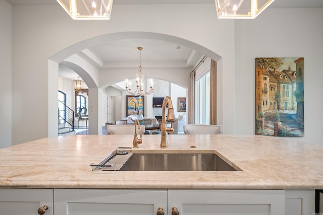 kitchen with white cabinetry, a notable chandelier, a tray ceiling, and a sink