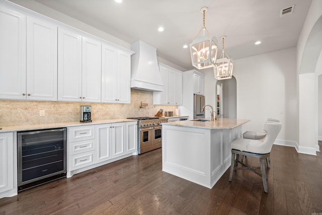 kitchen with wine cooler, a notable chandelier, custom exhaust hood, arched walkways, and appliances with stainless steel finishes